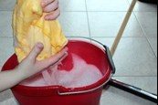 A person cleaning the floor with a bucket of soapy water and a sponge